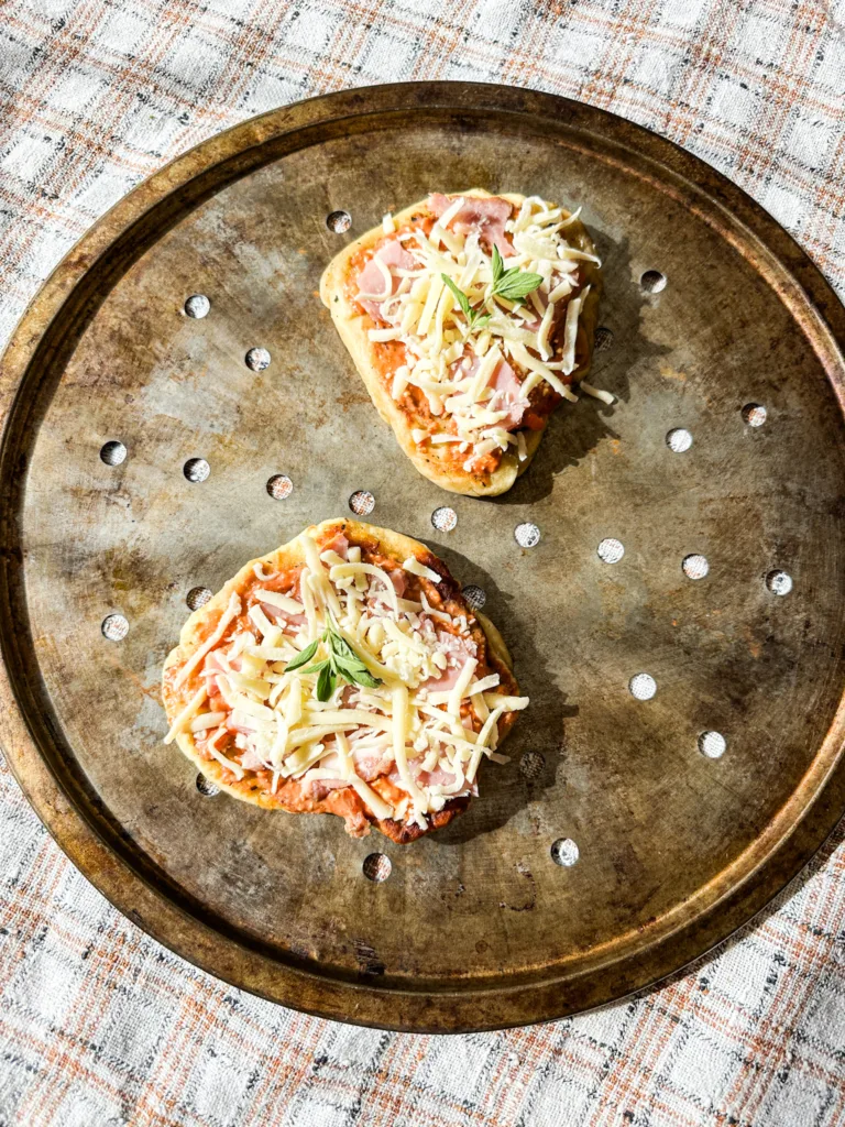 Two pieces of naan pizza on a round pizza pan.