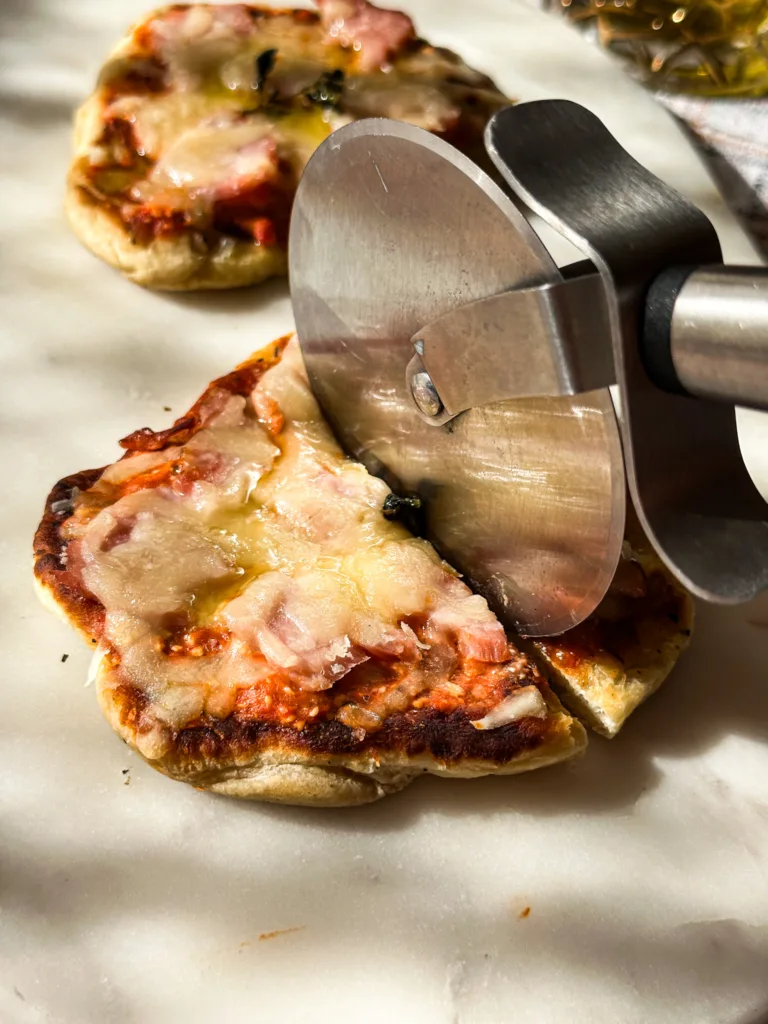 Naan pizza being cut with a pizza cutter.