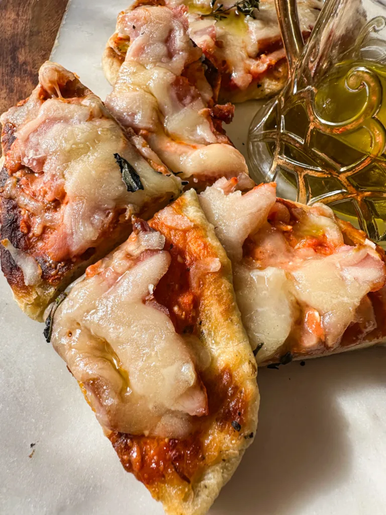 Naan pizza on a cutting board next to some olive oil.