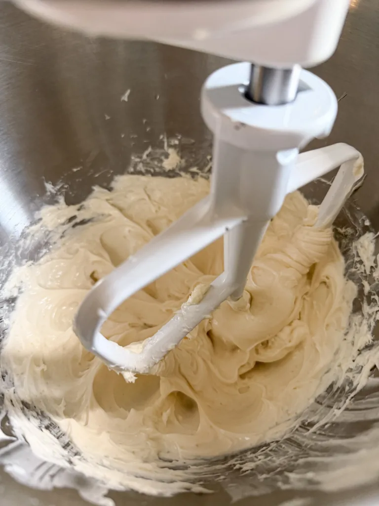 A stand mixer with a paddle attachment mixing a cream cheese mixture.