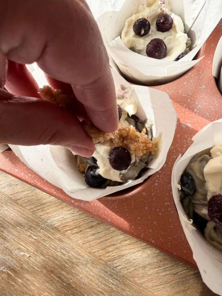 Streusel being sprinkled onto blueberry cream cheese muffins.