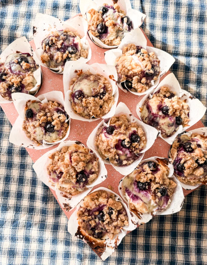 Finished blueberry cream cheese muffins in a muffin tin on a table cloth.