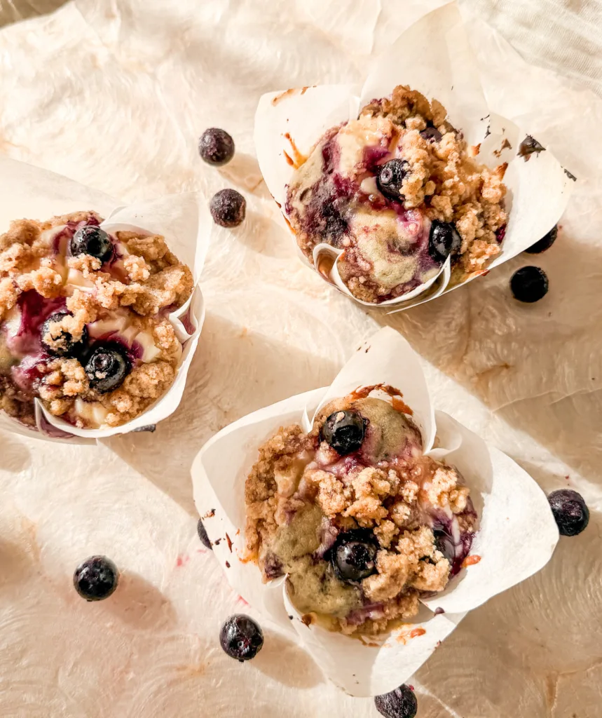 Blueberry cream cheese muffins on a placemat, next to blueberries.
