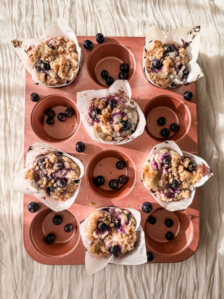 Blueberry cream cheese muffins in a muffin tin with blueberries.