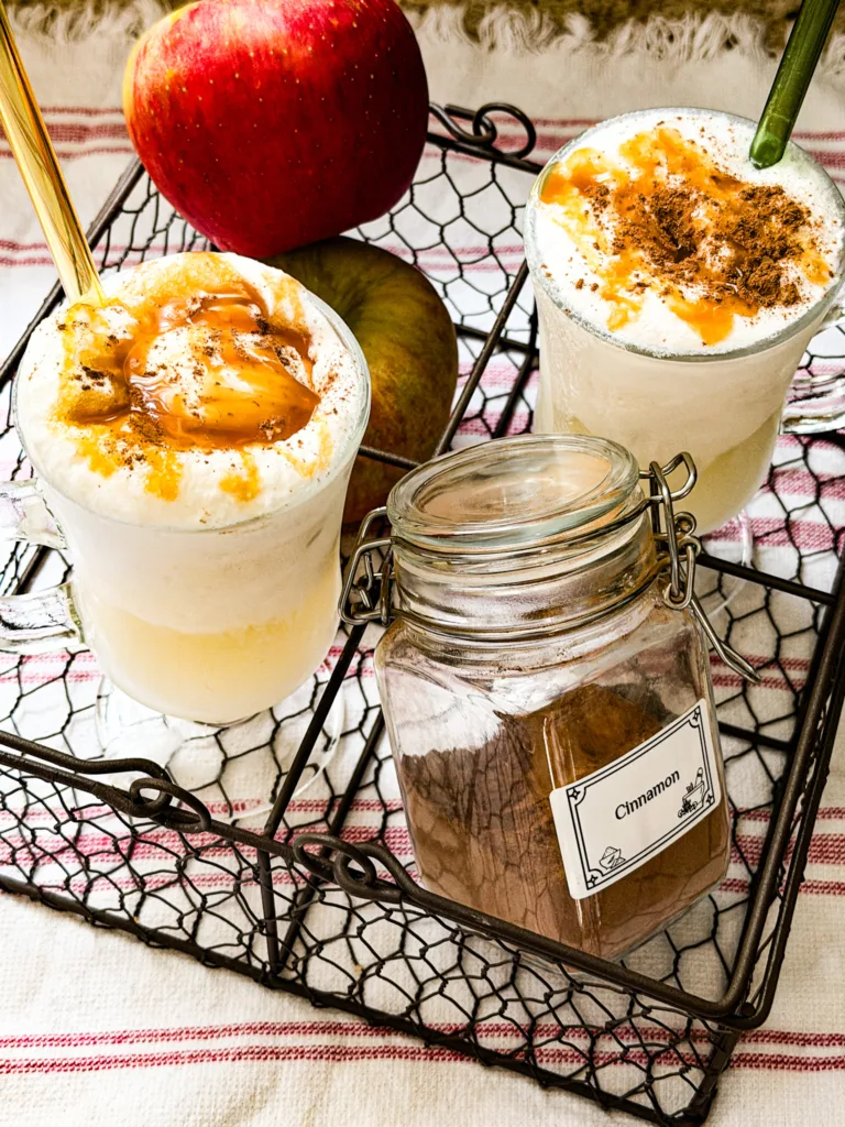 A wire cady with a jar of cinnamon, apples, and two glasses of apple dirty soda floats.