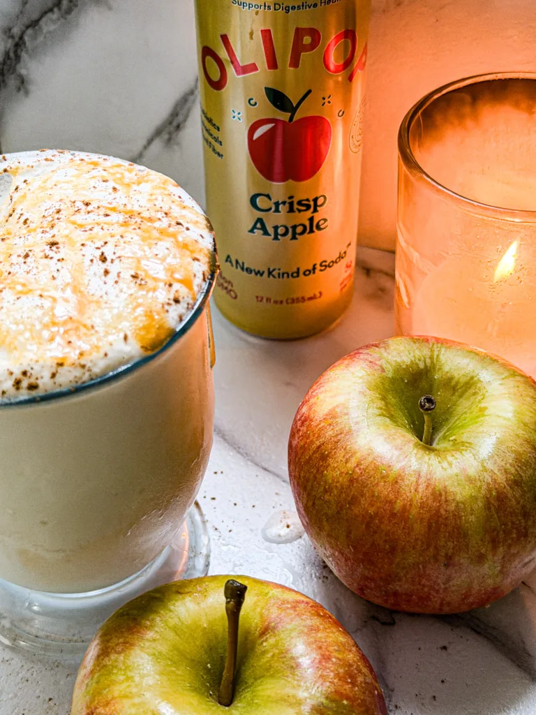 A can of pop next to a candle, apples, and a cup of apple dirty soda float.